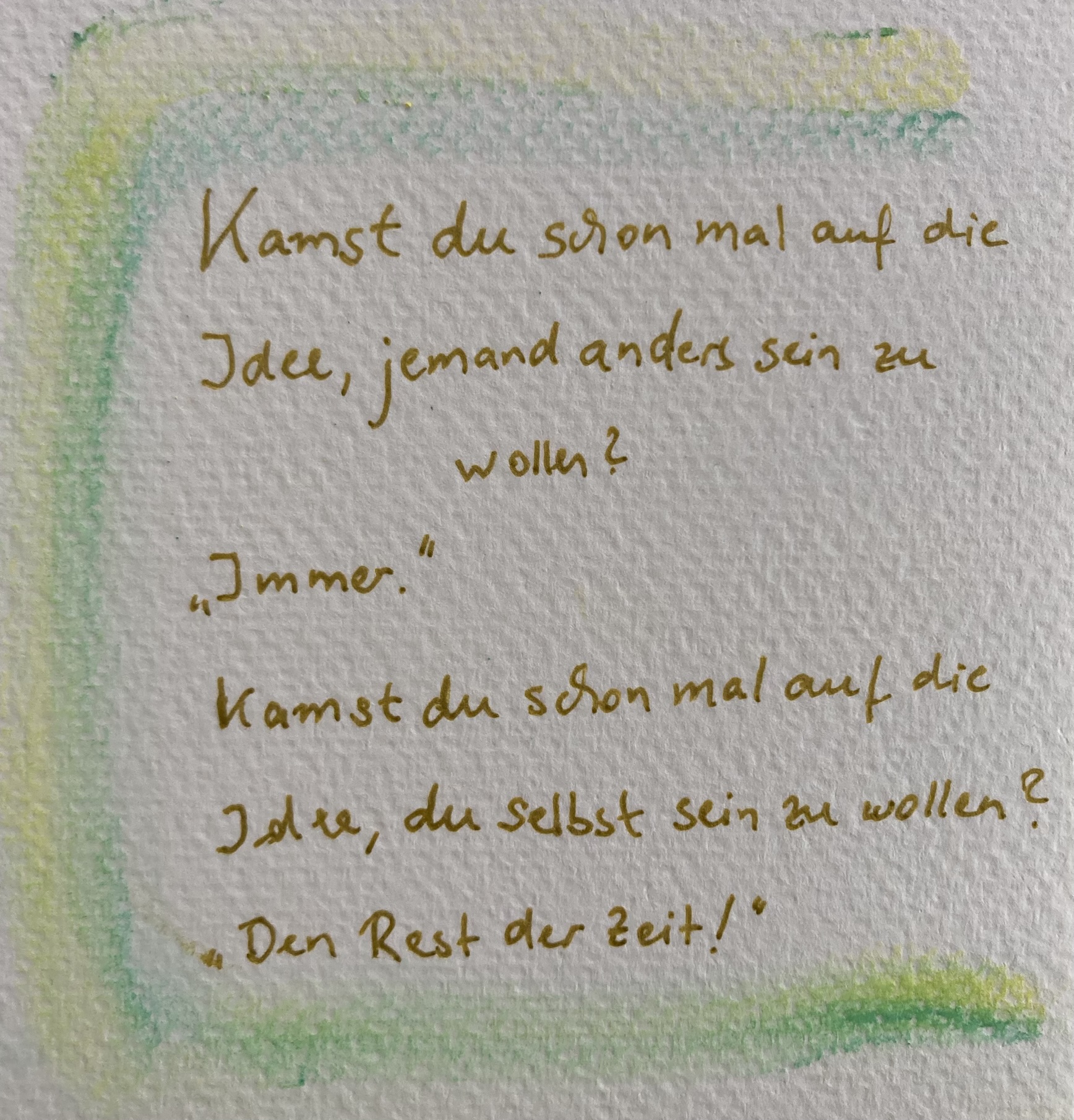 Auf Aquarellpapier ist ein blasser Rahmen aus Gelb und Grün fingergemalt, darin steht mit Goldstift geschrieben: "Kamst du schon mal auf die Idee, jemand anders sein zu wollen?" "Immer!" "Kamst du schon mal auf die Idee, du selbst sein zu wollen?" "Den Rest der Zeit!"