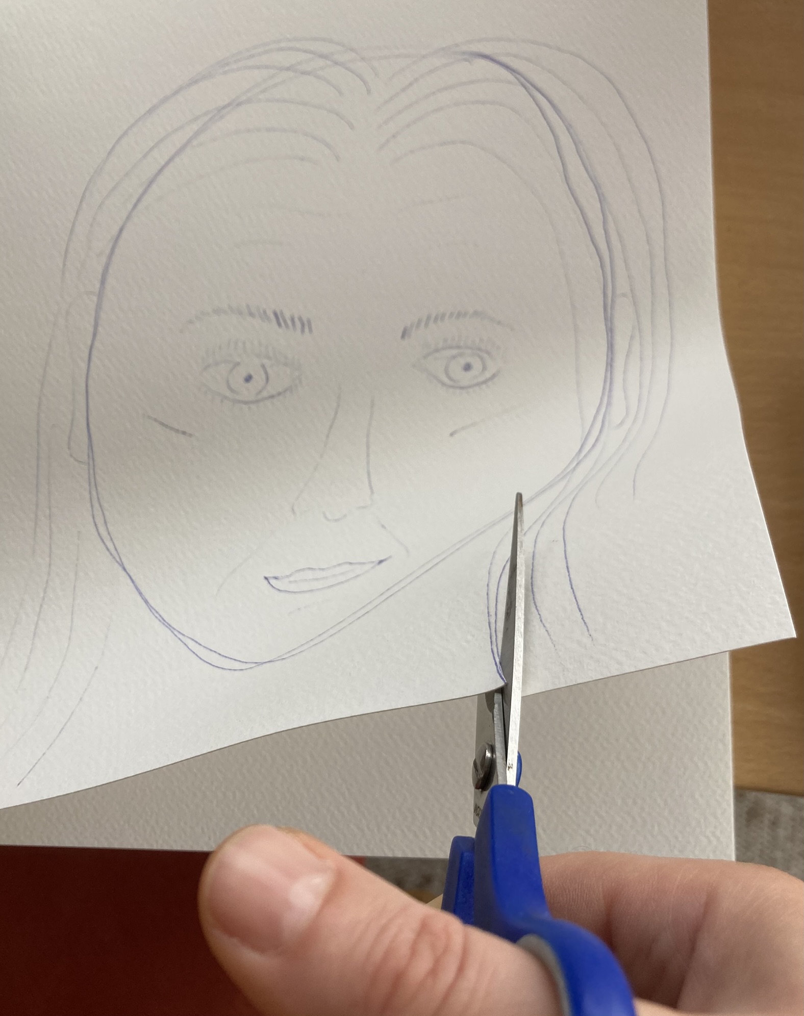 Das mit Kugelschreiber skizzierte Gesicht wird rechts unten an der Profillinie vom Hals mit einer blauen Schere eingeschnitten.