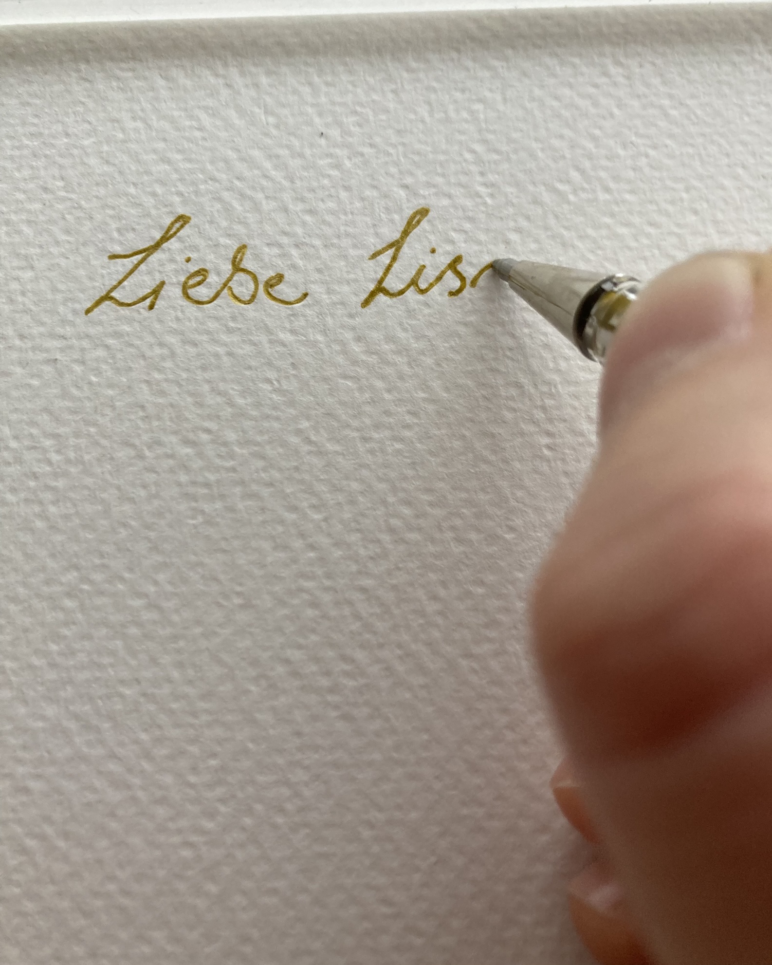 Auf einem schönen Papier schreibt eine Hand "Liebe Lis..." mit einem Goldstift.