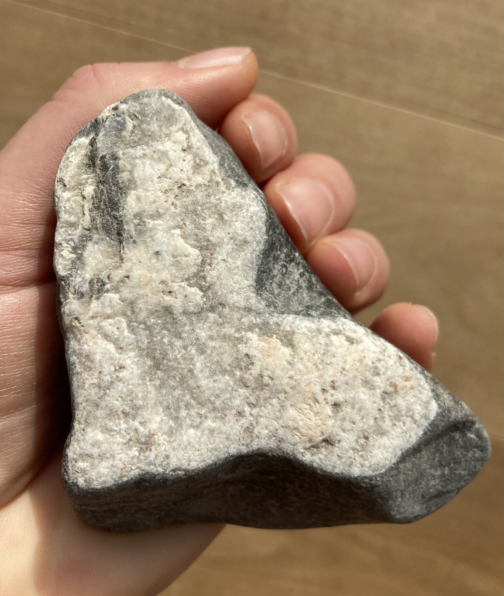 Eine linke Hand hält von unten einen handgroßen Stein in Herzform fest.