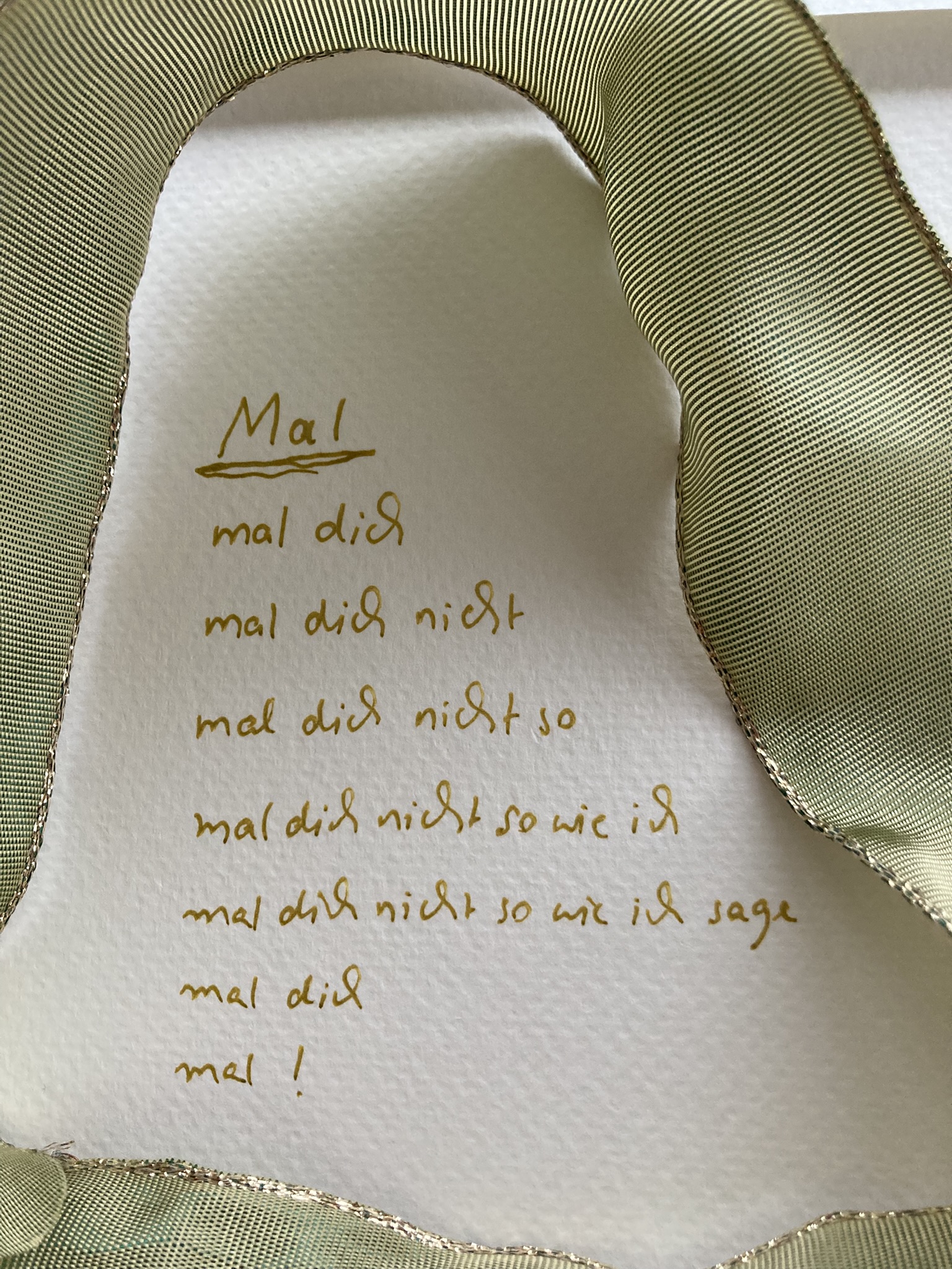 Von einer grünen Schleife umrandet steht auf Aquarellpapier mit Goldstift ein Gedicht.