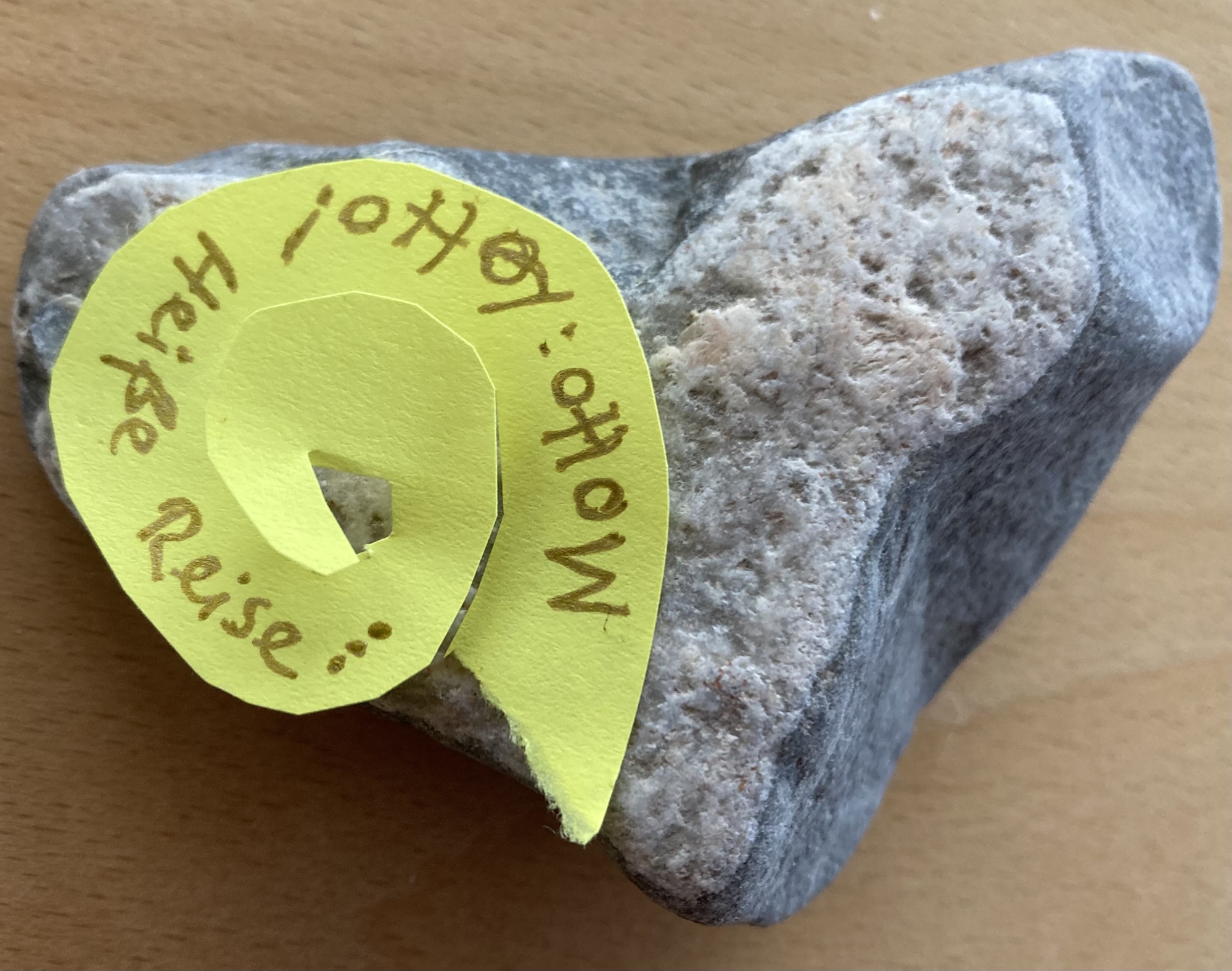 Auf einem Stein in Herzform klebt ein gelber Kringel mit den Worten: Motto: Lotto! Heiße Reise